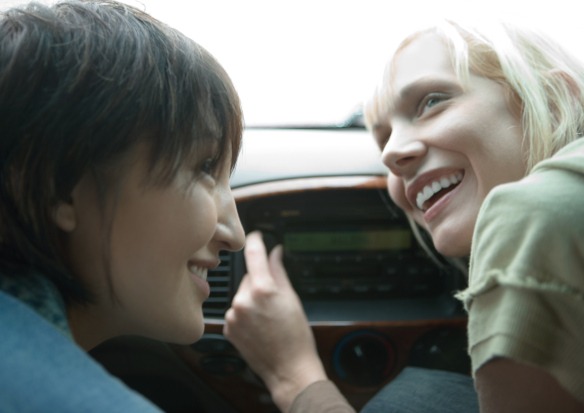 dwie kobiety w samochodzie słuchające radia przystawiając głowę do radioodbiornika sposoby na naukę języka słuchanie radia Preston Publishing