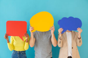 trójka młodych ludzi na niebieskim tle z zasłoniętymi twarzami trzymającymi kartony z dymkami dialogowymi w różnych kolorach jak uczyć się słówek Preston Publishing