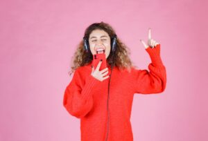 na różowym tle dziewczyna w czerwonej bluzie w słuchawkach śpiewa trzymając telefon w dłoni postanowienia noworoczne nauka języka obcego Preston publishing