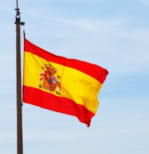 flaga Hiszpanii na tle niebieskiego nieba Fiesta Nacional de España, czyli Dzień Hiszpanii Hiszpańskie tradycje i zwyczaje Preston Publishing
