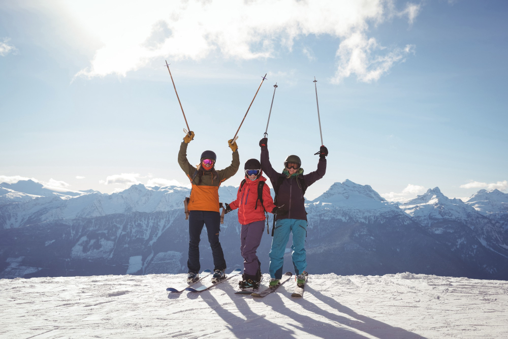 Trzech ludzi na stoku narciarskim z uniesionymi kijami narciarskimi