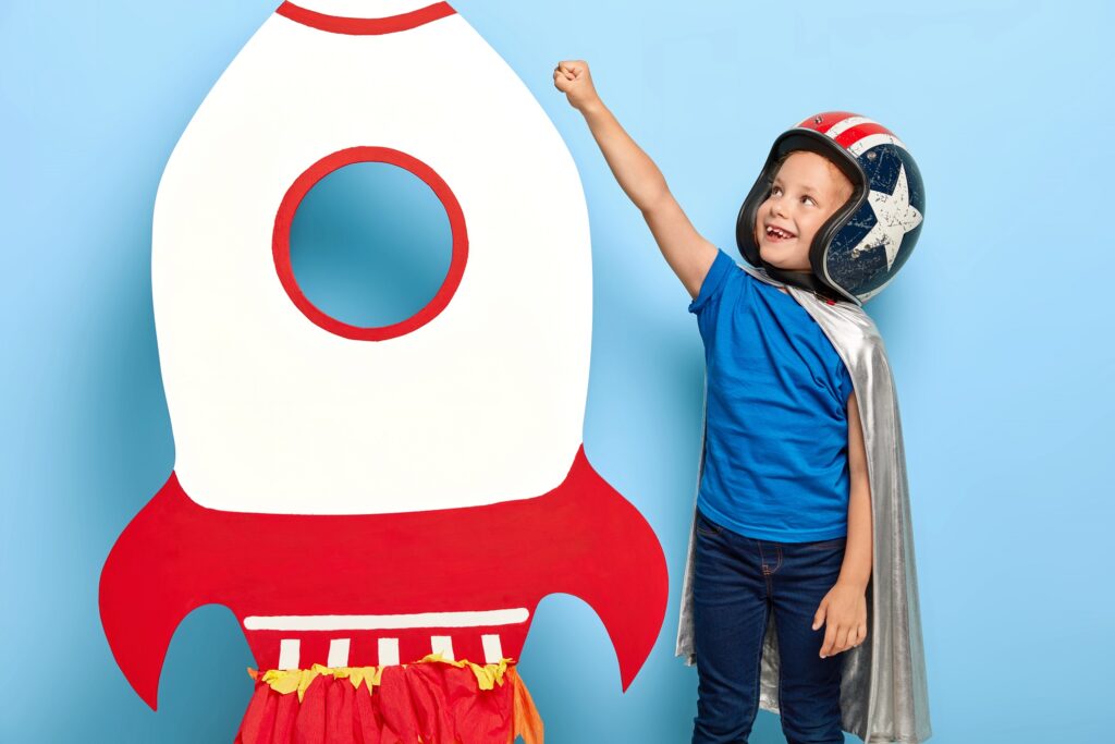 dziecko w stroju astronauty stoi przy kartonowej rakiecie książka angielski w przedszkolu gry i zabawy Preston Publishing