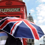 widok na Londyn w tle Big Ben czerwona budka telefoniczna na pierwszym planie ktoś stoi przed budka pod parasolka na ktorej jest wzór flagi brytyjskiej nauka czasów angielskich z książka angielski w tłumaczeniach od Preston Publishing