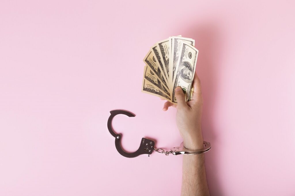 ręka mężczyzny trzymająca pieniądze zakuta w kajdanki na różowym tle borrow lend angielskie pulapki jezykowe Preston Publishing