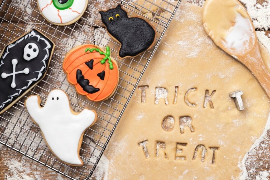 akcesoria do pieczenia ciasteczek halloweenowych i wykrojony z ciasta napis trick or Creat a obok gotowe ciasteczka w kształcie duchów dynii i innych motywów halloweenowych nauka języków obcych halloween w różnych krajach Preston Publishing