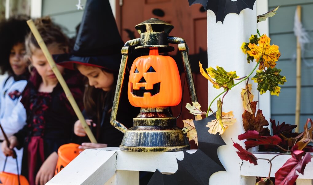 halloweenową ozdoba w postaci dynii wbudowanej w osłonę starej lampy naftowej a w tle dzieci i tradycja trick or treating