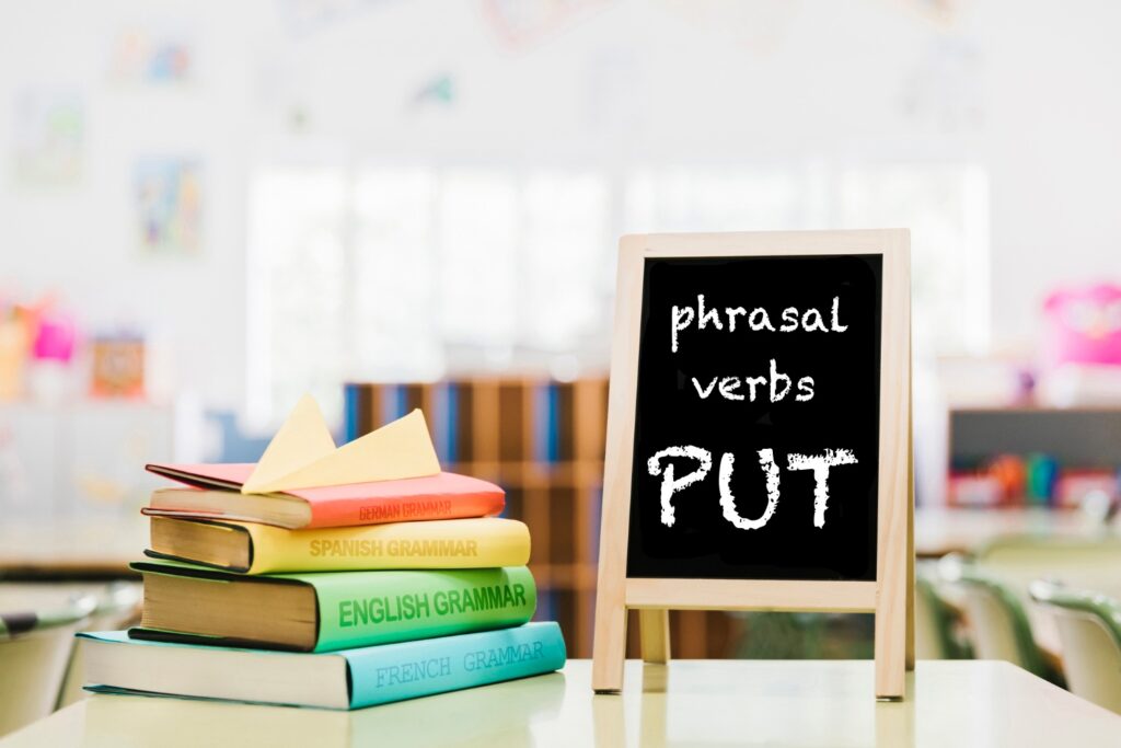 biurko w pokoju na którym leżą kolorowe książki oraz tabliczka do pisania kreda z napisem phrasal verbs aut nauka angielskiego czasowniki frazowe Preston Publishing