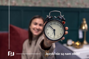 uśmiechnięta dziewczyna z wyciągniętym w dłoni budzikiem Czasy w języku hiszpańskim: Pretérito Perfecto Preston Publishing