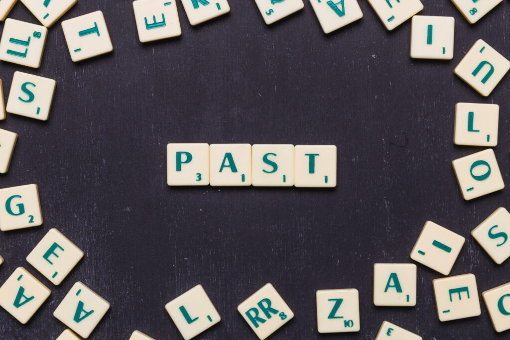kostki z literkami do gry w scrabble rozsypane na czarnym stole a cztery układają się w napis past nauka czasów angielskich Preston Publishing