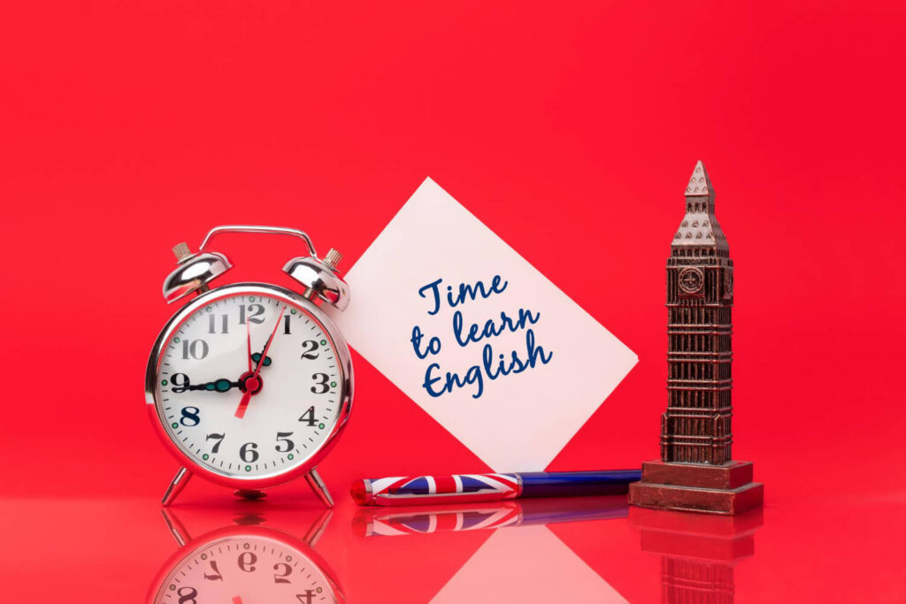 na czerwonym tle budzik figurka Big Bena oraz karteczka z napisem time to learn english czas na naukę angielskiego angielskie czasy Preston Publishing