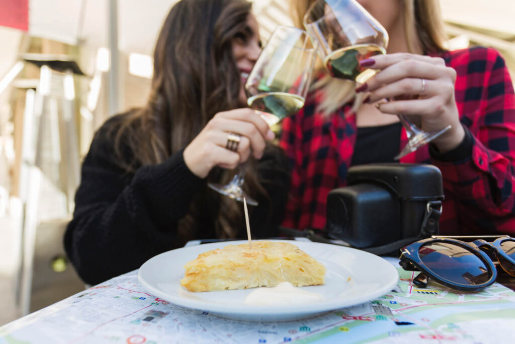 dwie osoby stukające się kieliszkami z winem przy stoliku z deserem zamawianie napojów w restauracji po hiszpańsku Preston Publishing