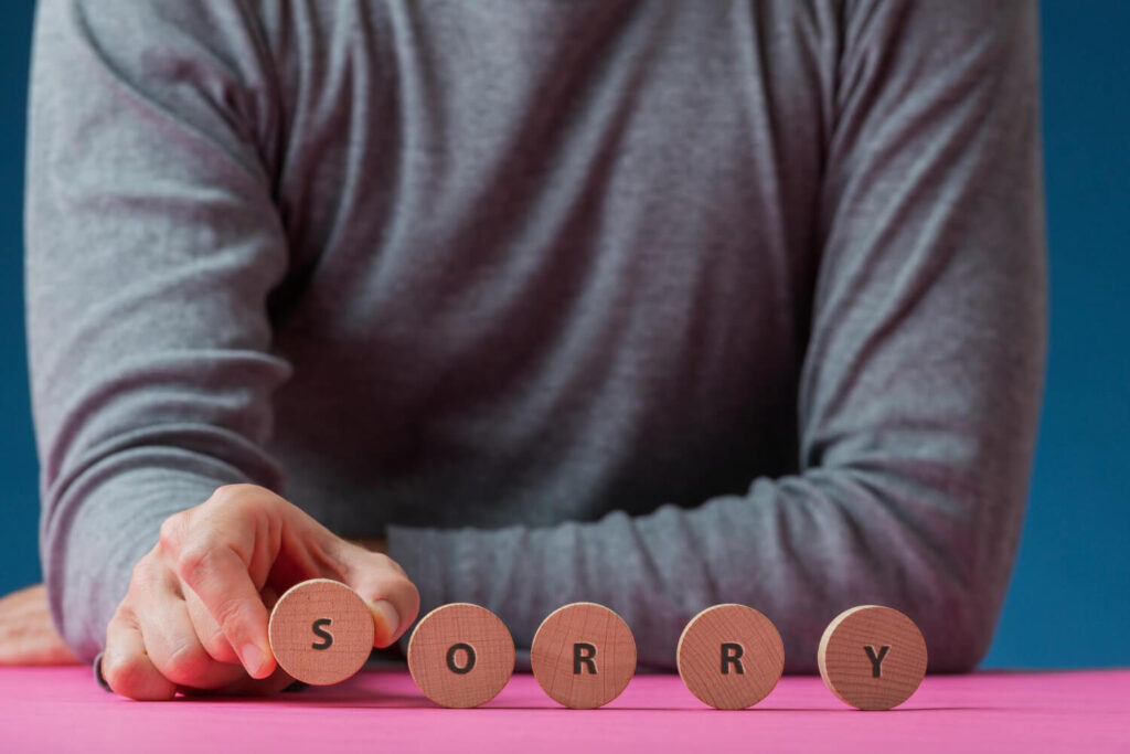 mężczyzna siedzący przy stole i układający okrągłe klocki z literkami układającymi się w słowo sorry po angielsku przepraszam nauka języka angielskiego Preston Publishing