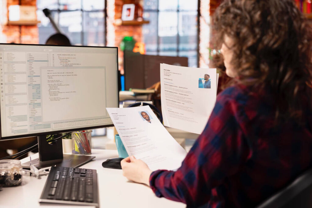 kobieta siedząca przy biurku oglądająca cv dwóch osób  jak napisać cv po francusku Preston Publishing