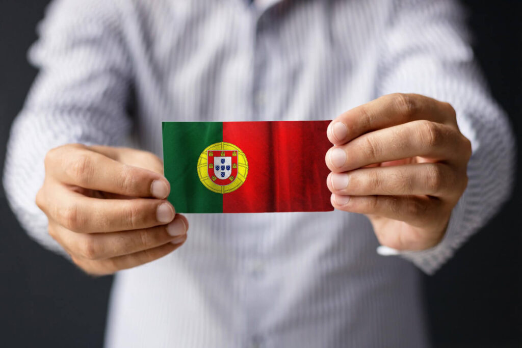 mezczyzna w koszuli trzymający w wyciągniętych rekach mała portugalska flagę nauka portugalskiego od podstaw Preston Publishing