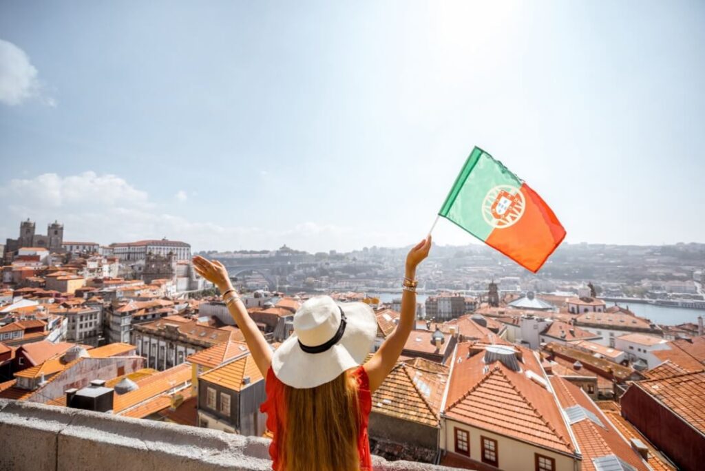 dziewczyna w kapeluszu z wyciągniętymi w gore rękami podziwia widok Lizbone trzymając portugalska flagę nauka portugalskiego od podstaw Preston Publishing