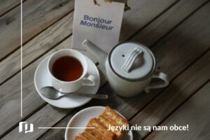 na stole filiżanka z herbata, croissant oraz cukiernica, a obok karteczka z napisem bonjour monsieur podstawowe zwroty po francusku powitania i pożegnania Preston Publishing