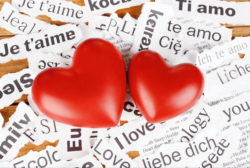 dwa czerwone serca na tle wycinków z gazety z napisami kocham cie w różnych językach nauka słownictwa z Preston Publishing