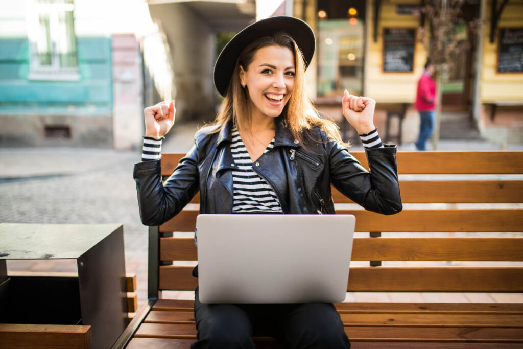 dziewczyna w kapeluszu i z laptopem ciesząca się z uniesionymi rękami w gorze nauka języka francuskiego z Preston Publishing