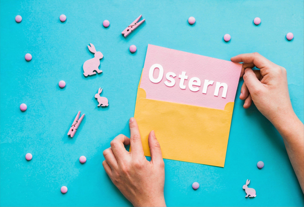 napis Wielkanoc po niemiecku na kartce która ktos wkłada do koperty a dookoła dekoracje nauka języków Preston Publishing