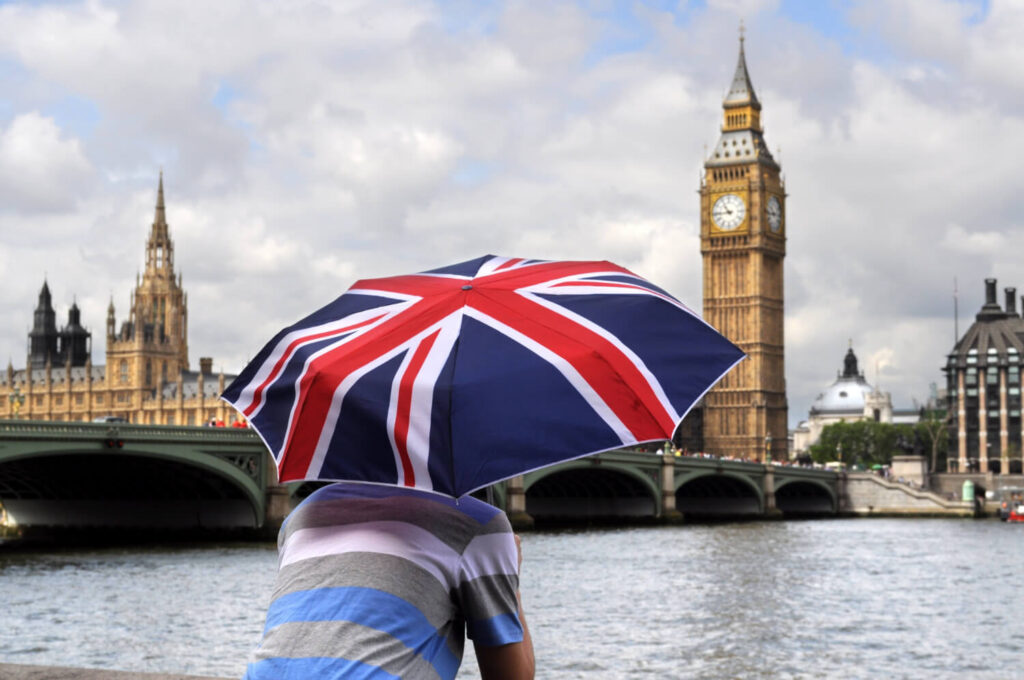 widok na Big Bena i opactwo westminsterskie z mostu na ktorym siedzi turysta z parasolka w kolorach brytyjskiej flagi nauka angielskiego z Preston Publishing