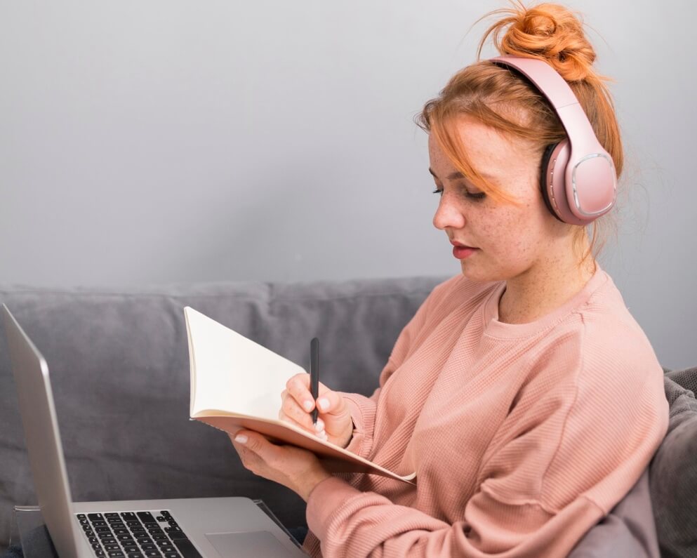 dziewczyna w sluchawkach przed laptopem i notatkami uczy sie jezyka z Preston Publishing odsluchujac nagrania do ksiazek