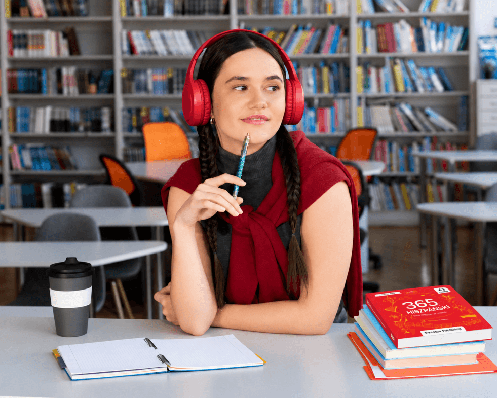 dziewczyna w czerwonych sluchawkach z  notatkami  i ksiazka do nauki hiszpanskiego jezyka uczy sie jezyka z Preston Publishing odsluchujac nagrania do ksiazki